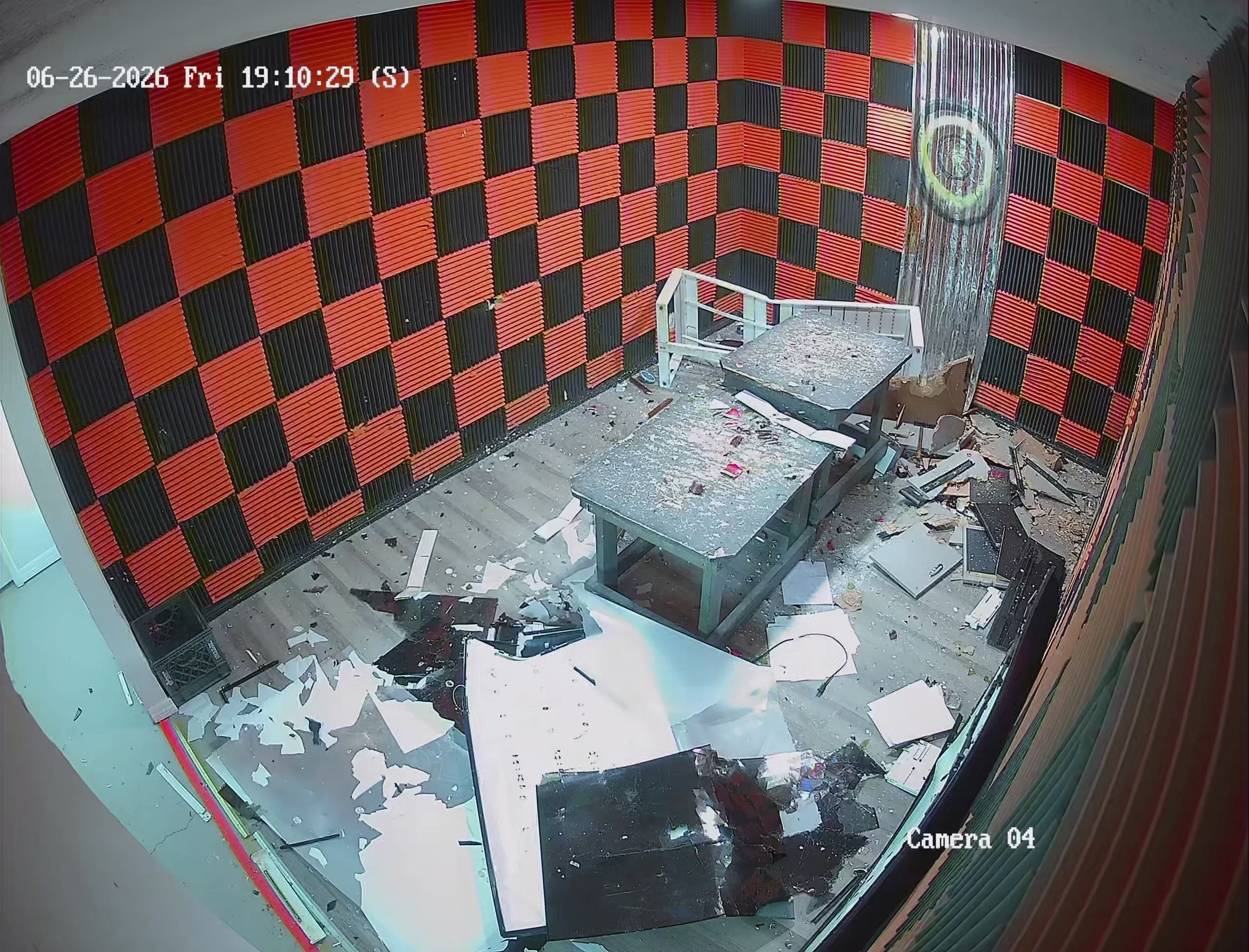 Security camera view of Crash Out smash room aftermath — completely demolished with shattered glass, broken screens, and debris covering the floor